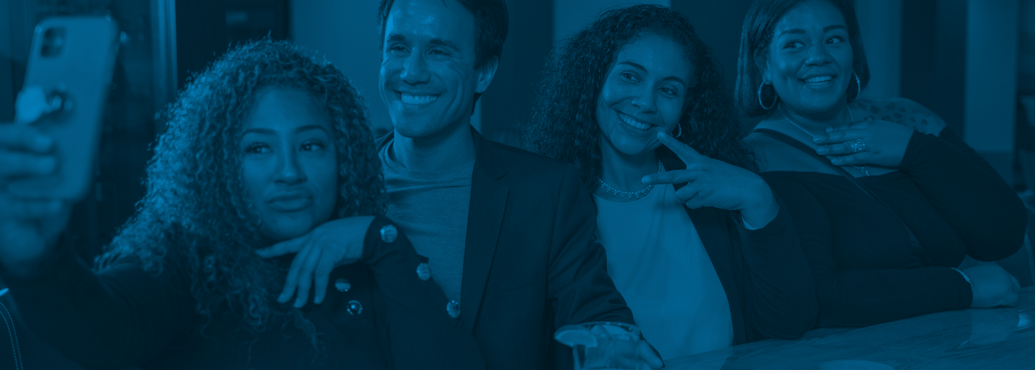 4 individuals taking a selfie with a phone sitting at a bar