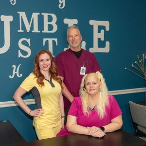 Three people in colorful scrubs smiling in front of a blue wall