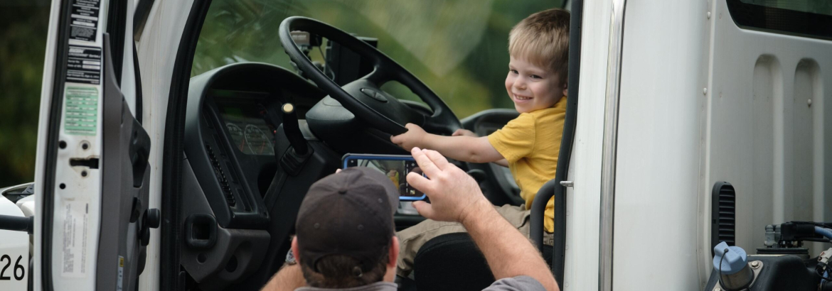 little boy sitting in the front seat of a truck and his dad taking a picture of him