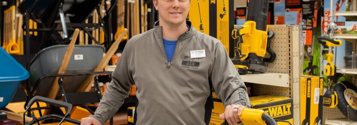 guy in grey pullover in a hardware store with yellow tools surrounding him